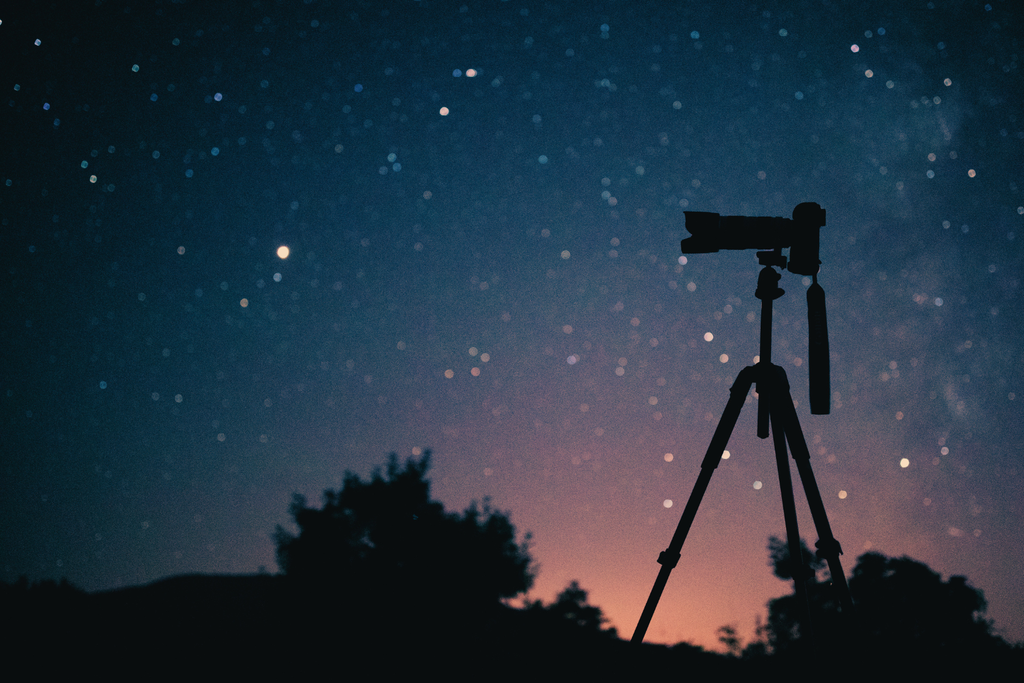 Photo d'un trépied de photo avec un ciel étoilé en fond pour illustrer l'analogie entre photo du ciel et thème astral. 